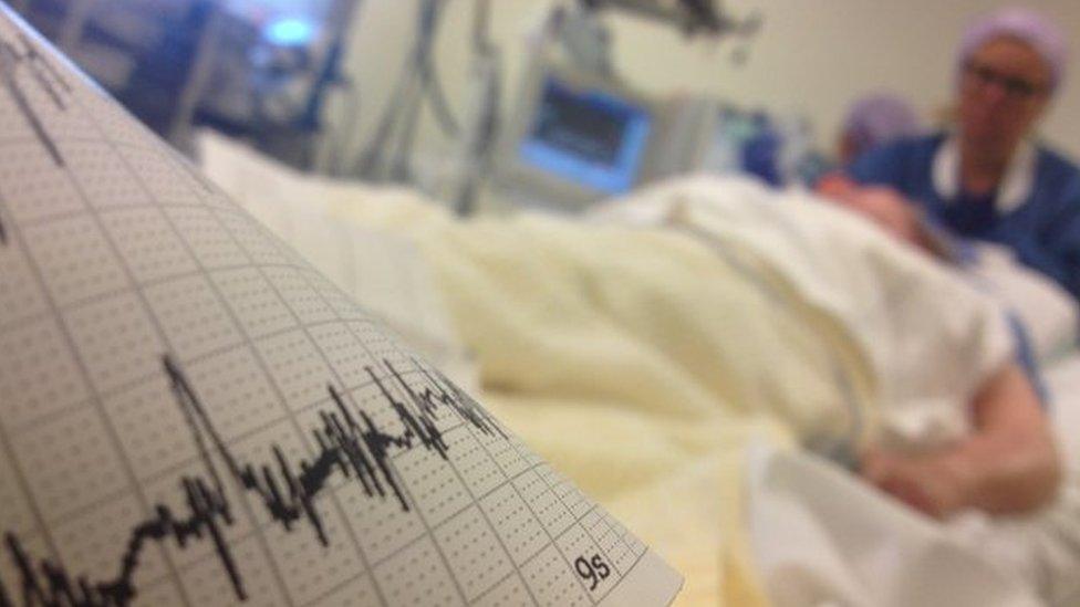EEG trace in foreground with patient on bed and woman in scrubs in background