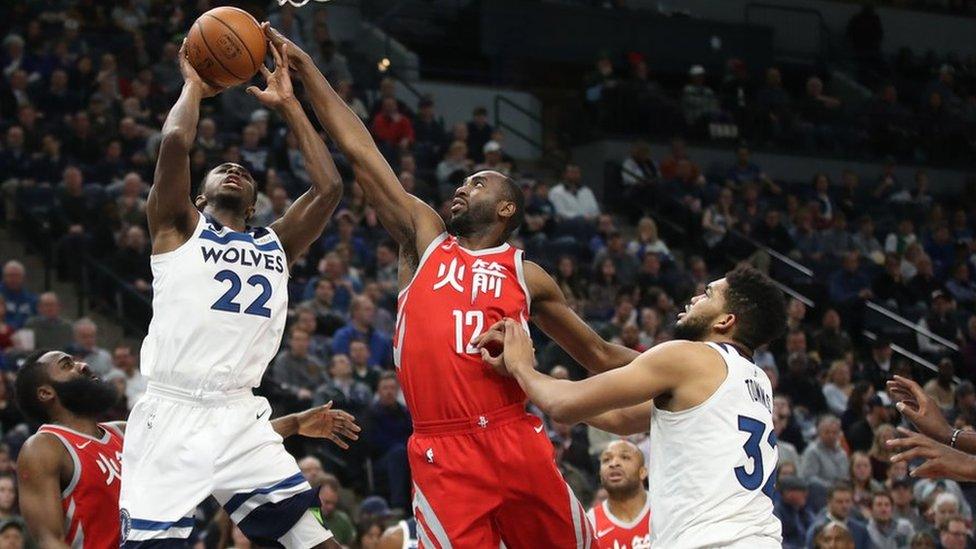 Basketball players struggle over the ball below a basket.