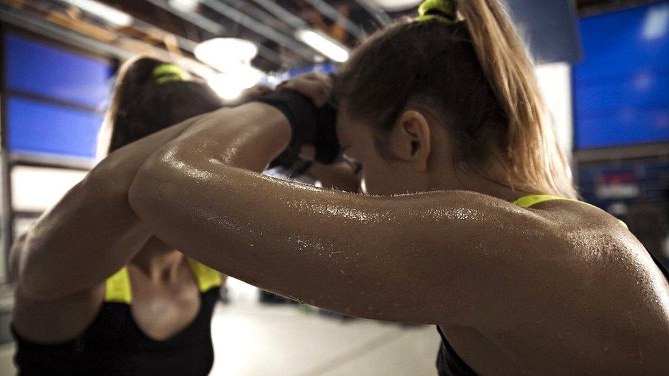 A woman who is sweating rests her head on her arm against a mirror