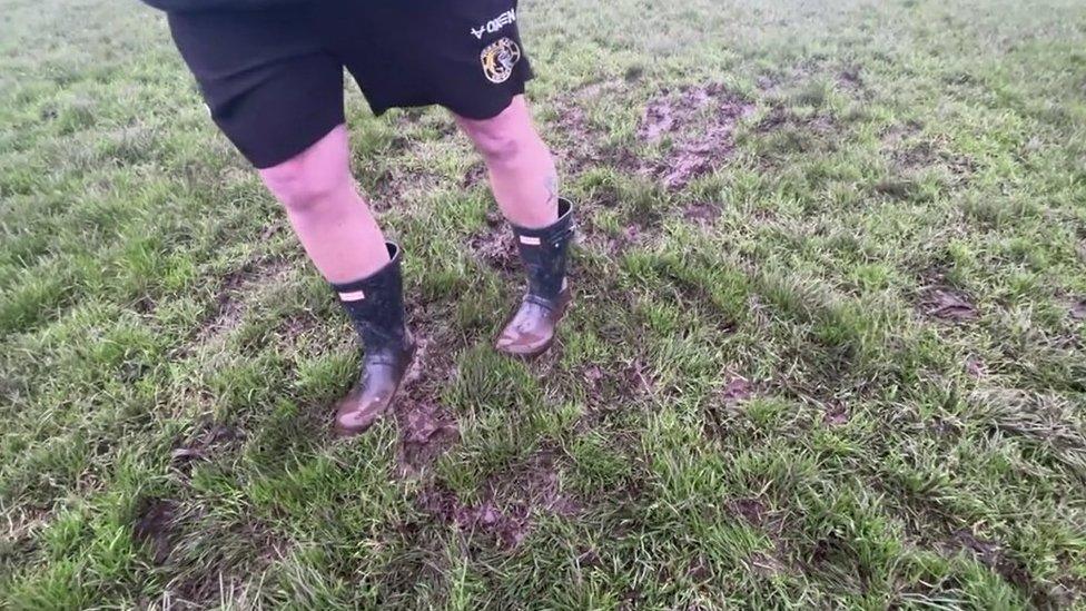 A member of the rugby club demonstrates how his feet would sink into the muddy grass