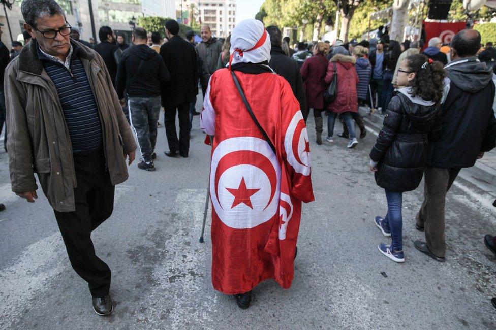 A woman draped in the national flag walks down a road on the anniversary of the 2011 Arab Spring.