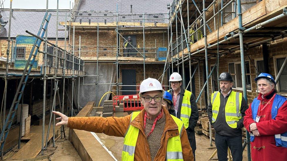 Old derelict building surrounded by scaffolding and four men in hard hats