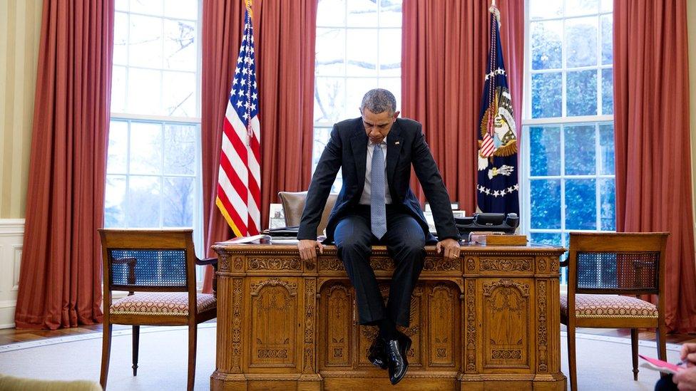 Barack Obama sits on his desk in the Oval Office, deep in thought