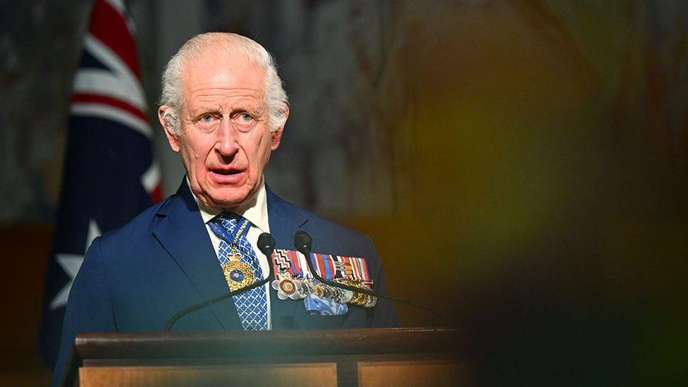 King Charles delivers a code   successful  the Australian Parliament connected  21 October. He is wearing a suit   and achromatic  garment  with a bluish  and achromatic  tie, with respective  medals connected  his near  lapel and a golden  necklace astir   his neck. He's looking somewhat  distant  from camera, with an out-of-focus assemblage  subordinate   successful  the foreground and an Australian emblem  successful  the background.