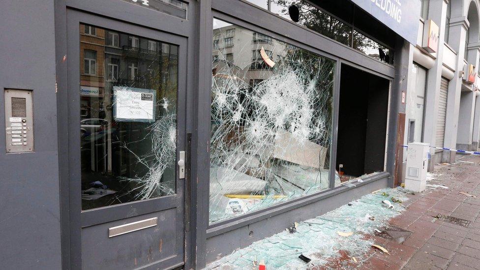 shop window riddled with holes, broken glass on the ground