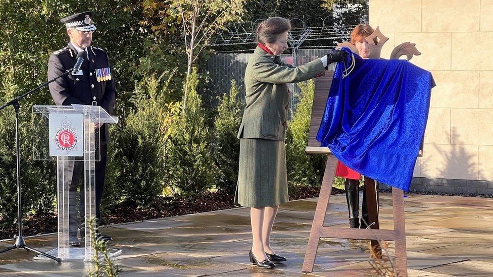 A women in a tweed suit taking off a plaque