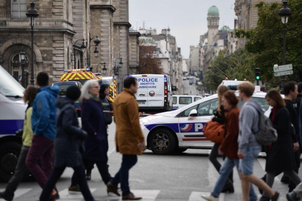 Passerby walk as police vehicle drive toward Paris after a fatal knife attacks.