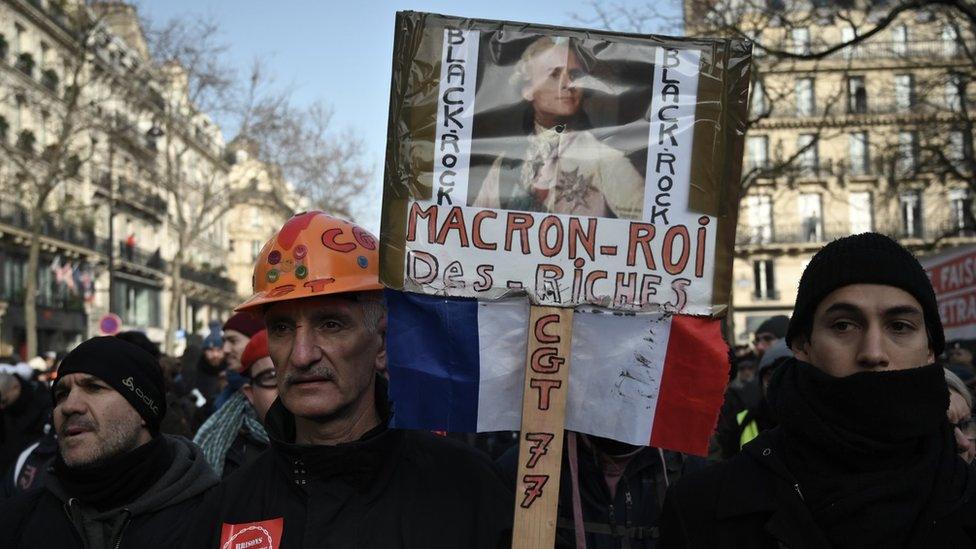 A man holds a placard reading "Macron king of the rich people" in Paris on January 24, 2020 during a demonstration against the government pensions reform