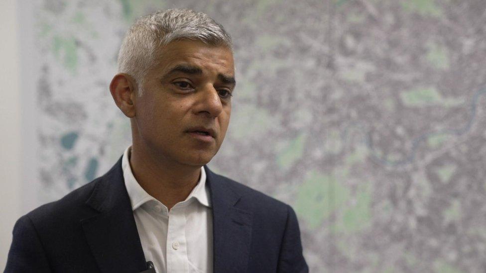 Sadiq Khan speaking in front of a grey and green backdrop.