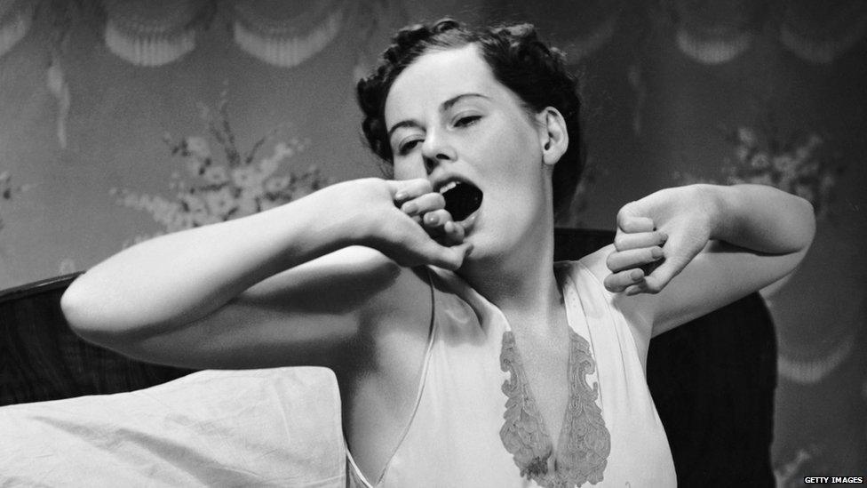 Black and white photo of a woman in bed yawning