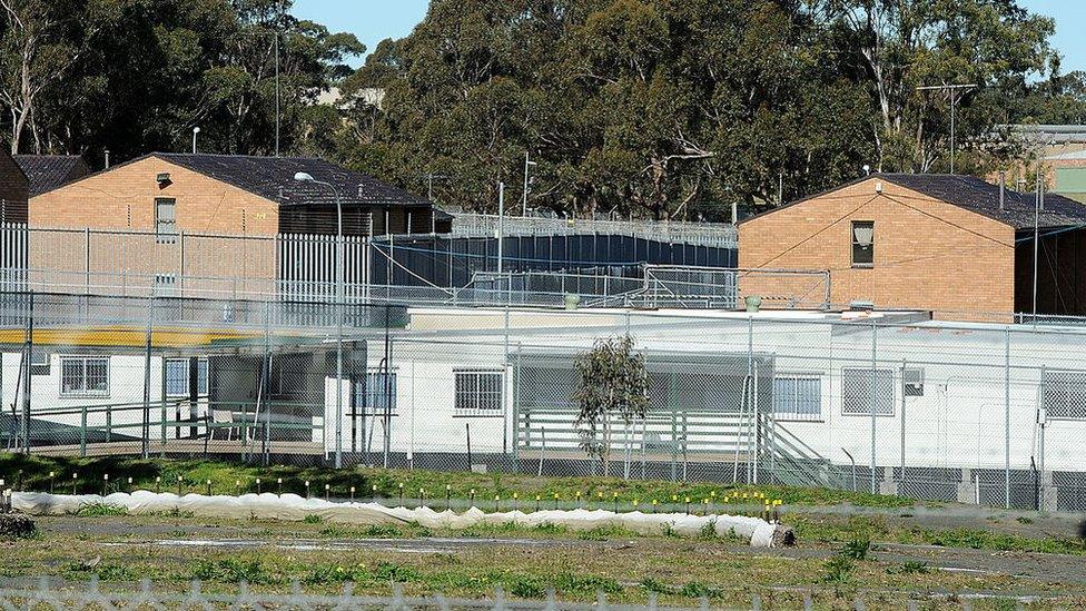 An external view of Villawood Immigration Detention Centre, showing two brick buildings enclosed by high fences