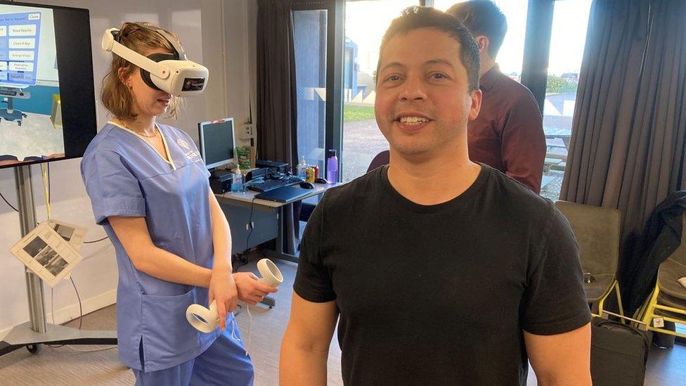 Aziz Naji standing in front of a medical student in blue scrubs using the VR headset