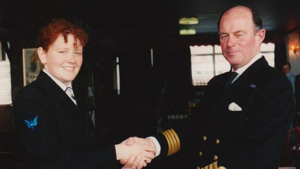 A woman smiles at the camera as she shakes the hand of a colleague