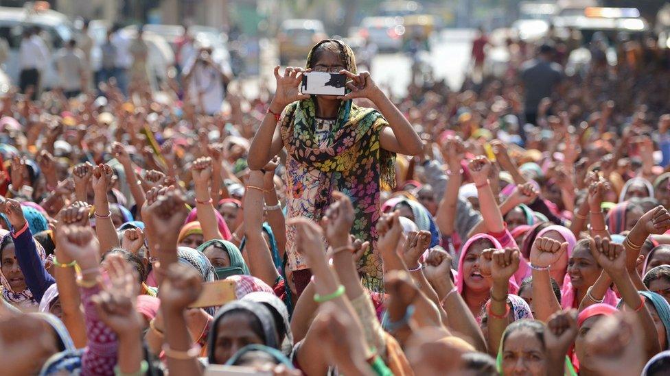 A woman from an Indian workers' union takes photos on a mobile phone during a protest in Ahmadabad on February 12, 2017.