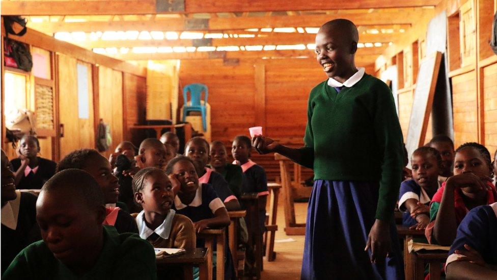 A girl holds up a cup in a class room at one of Ruby Cup's African projects