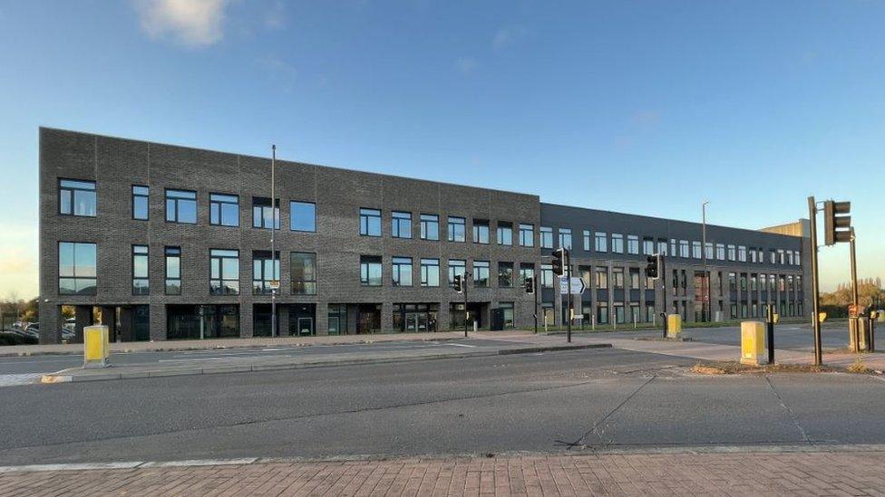 The Deanery CE Academy. It is a large modern brick building with lots of windows next to a road