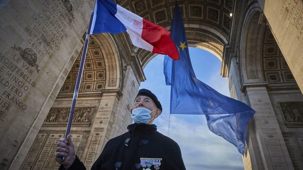 A veteran stands with the French flag next to a giant flag of the European Union at the Arc de Triomphe on January 01, 2022 in Paris, France.