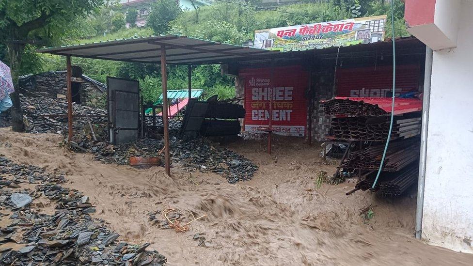 Water gushes by a shed and building in Pipalkoti village in Chamoli district in Uttarakhand