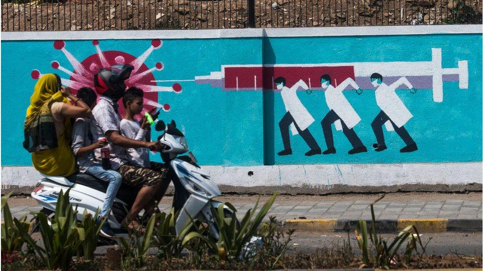 People walking past a wall mural depicting Medical staff hitting Corona with Vaccine Needle