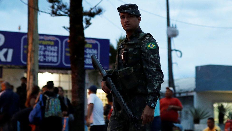 An army soldier patrols on a street next to people from Venezuela