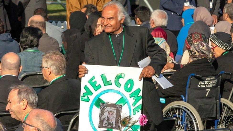 A man holding a sign saying "welcome" for the family members of victims of the Christchurch mosque shootings