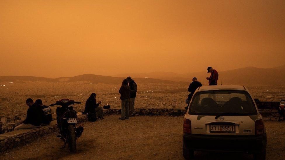 People sit on Tourkovounia hill overlooking the city of Athens, as southerly winds carry waves of Saharan dust to the city, in Athens, on April 23, 2024