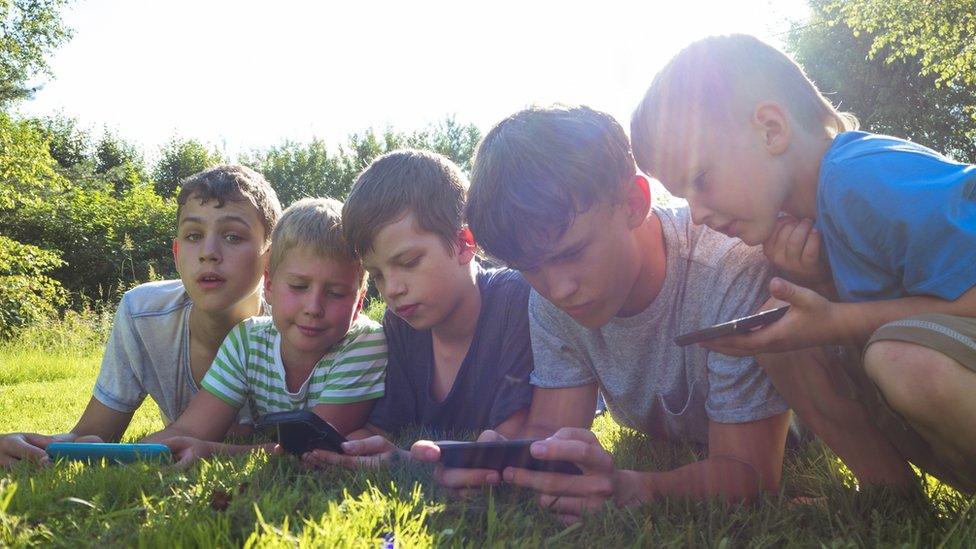 Children of varied ages looking at screens outdoors