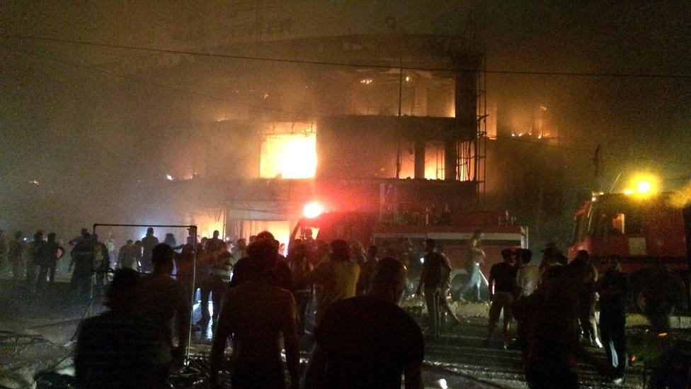 Iraqi firefighters try to extinguish a fire as civilians gather after a car bomb at a commercial area in Karrada neighbourhood, Baghdad, Iraq, early Sunday, July 3, 2016.