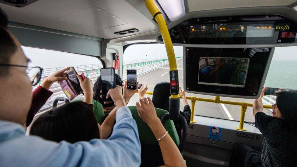 Passengers take photos in a bus being driven towards Macau