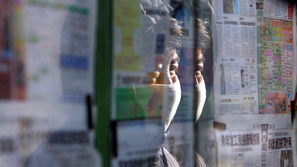 Masked woman reads the news from state-controlled newspapers posted behind glass enclosures on a Beijing street