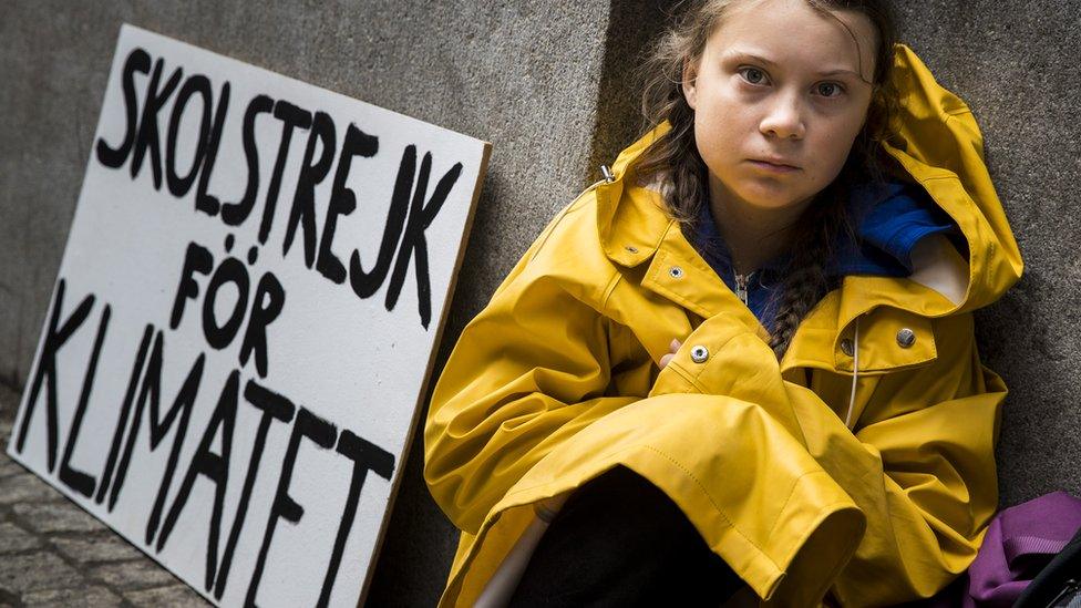 Greta Thunberg sits next to her school strike for climate sign