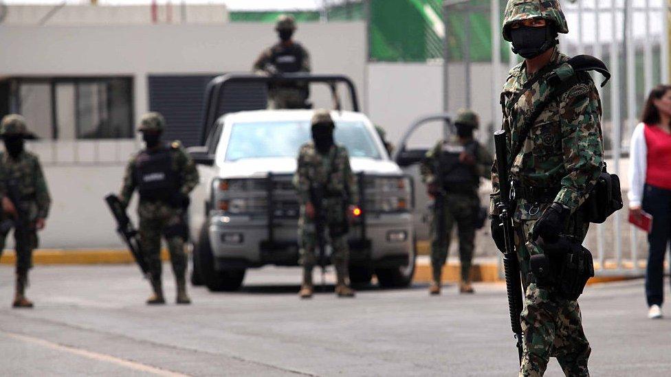 Armed police in helmets and camouflage suits stand in front of a vehicle on the street