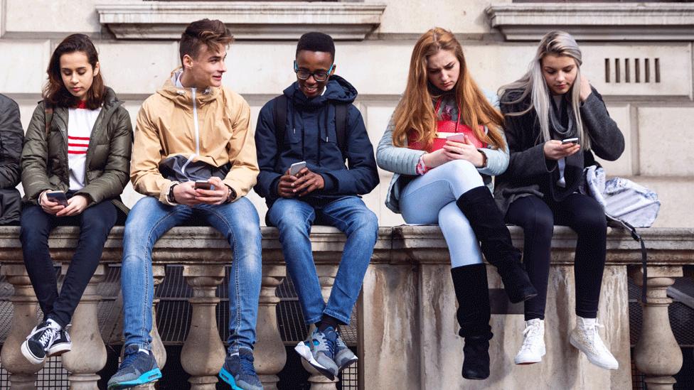 Teens on phones on a wall