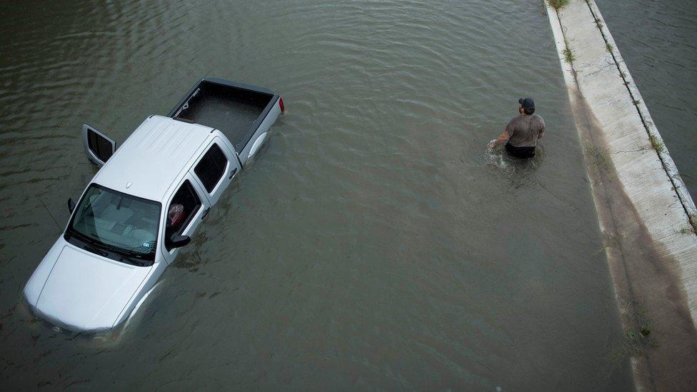 A truck driver walks past an abandoned truck while checking the depth of an underpass in Houston