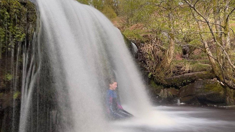 A woman sits under a waterfall