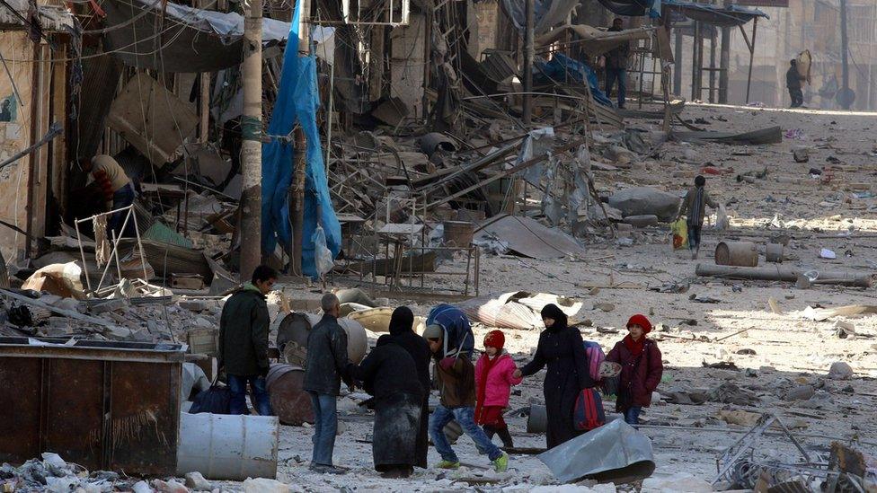 Syrians walk over rubble of damaged buildings in eastern Aleppo