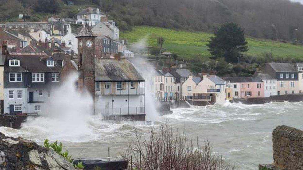 Waves crash against some buildings on a coastline.