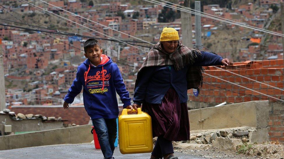 A woman and a child carry a bucket of water collected from a truck provided by officials of the Bolivian public water company, 22 November 2011