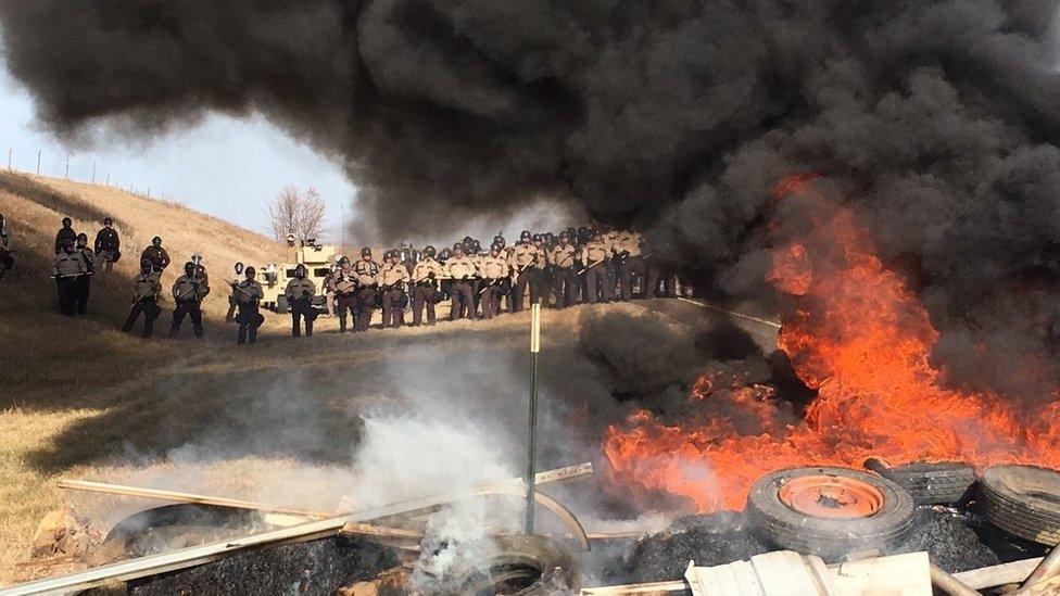 Tires burn as armed soldiers and law enforcement officers stand in formation on Thursday, Oct. 27, 2016, to force Dakota Access pipeline protesters off private land where they had camped to block construction.