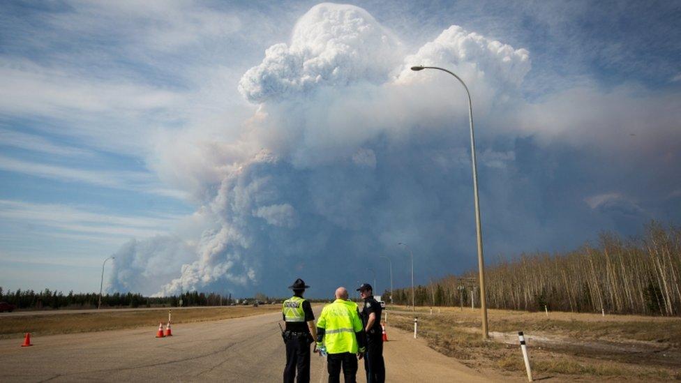 Police officers look as smoke billows from a wildfire in Fort McMurray, Canada. Photo: 4 May 2016