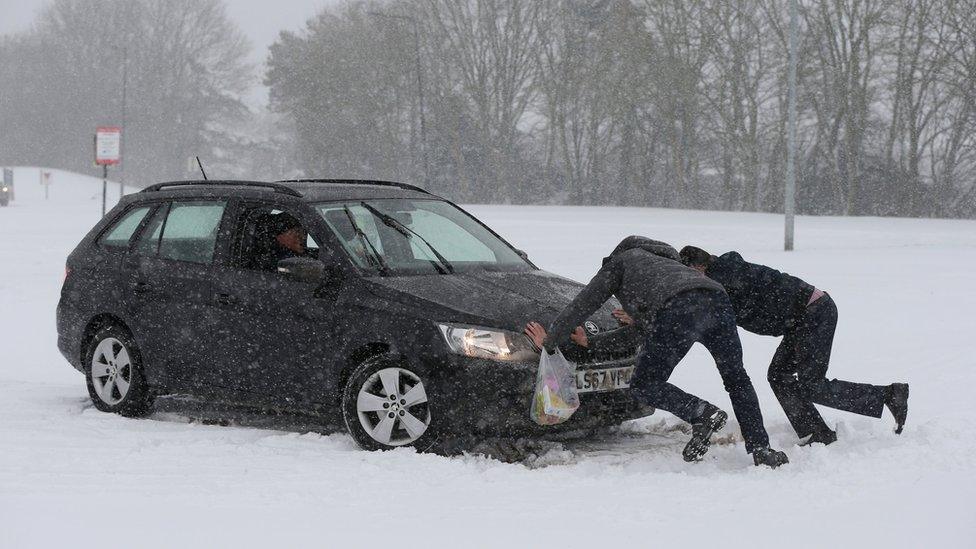 Two men push to help a driver try to get his car moving