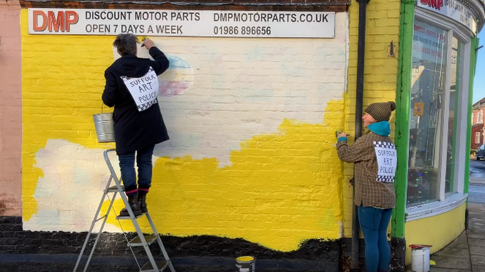 Member of the theatre company painting over a mural