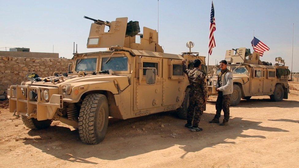 Syrian Democratic Forces fighters standing near US military vehicles on the outskirts of the Syrian town of Manbij (7 March 2017)