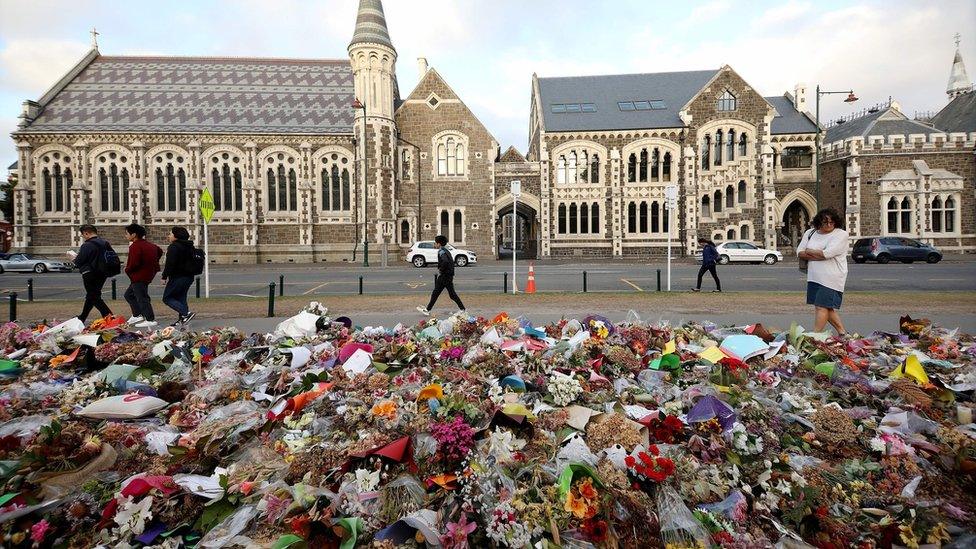 People walk past flowers and tributes displayed in memory of the twin mosque massacre victims outside the Botanical Gardens in Christchurch