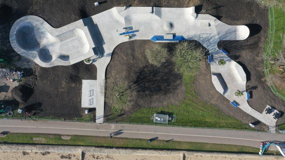 Aerial view of the skatepark, which is a light coloured concrete snaking through grass and trees beside the coastal path and beach