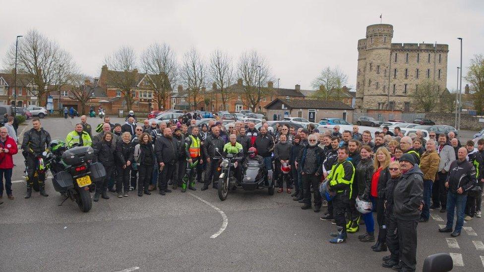 More than 100 people wearing motorcycle gear standing in a car park