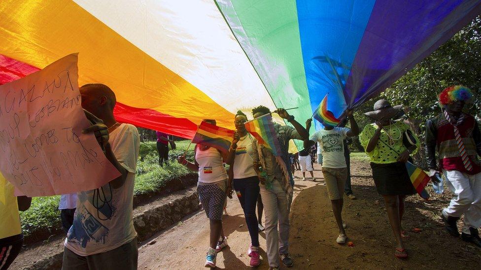 People walk under a giant rainbow flag as they take part in the Gay Pride parade in Entebbe on 8 August 2015.