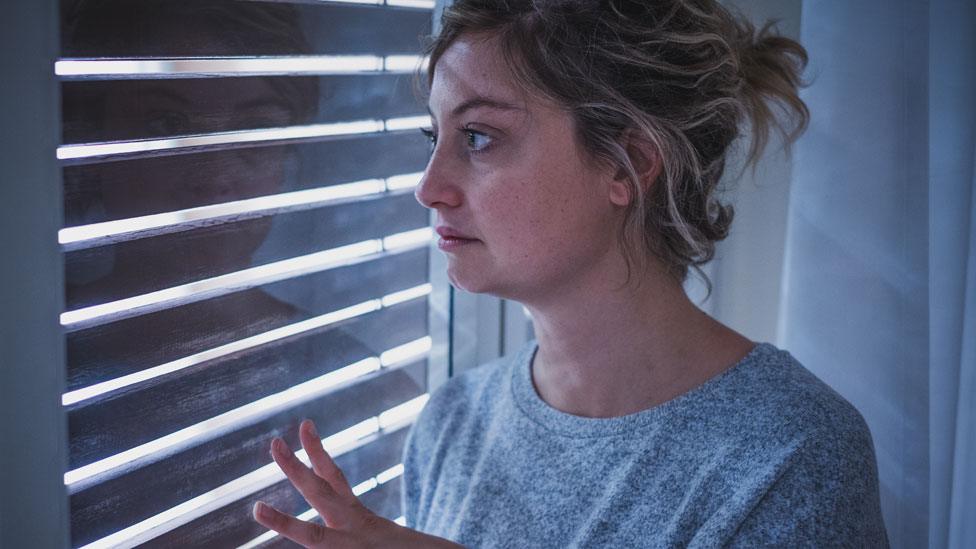 A stock image of a woman standing at a window