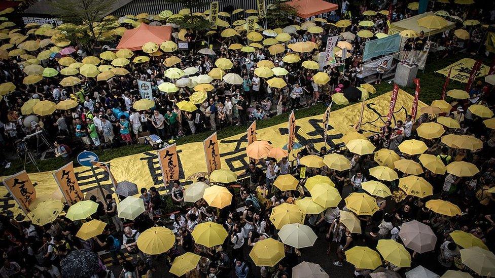 Pro-democracy demonstrators and activists gather outside the government headquarters building to mark one year since the start of mass pro-democracy rallies