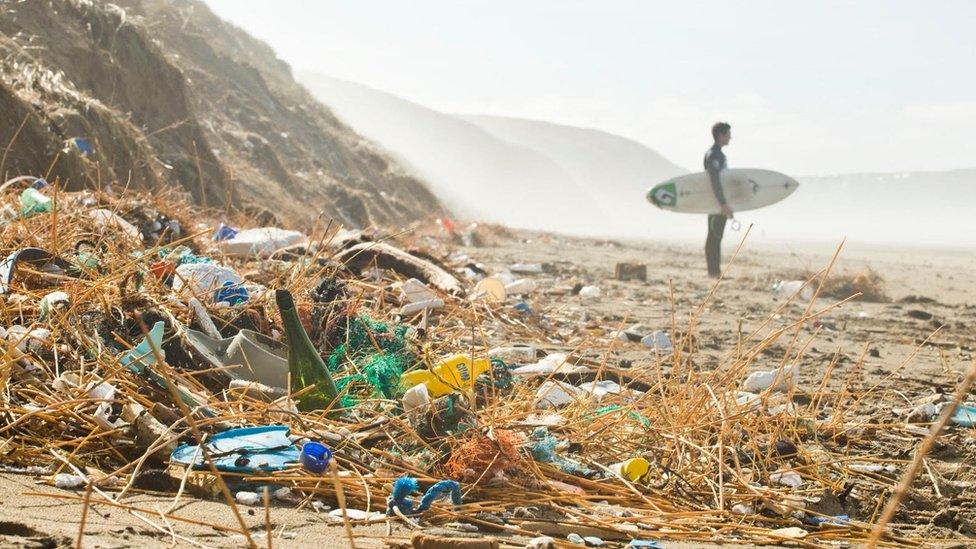 A surfer stands near a mound of plastic litter on a beach in Cornwall